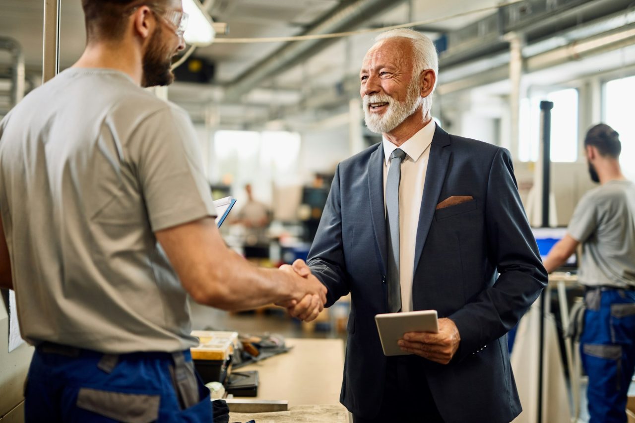 happy senior businessman handshaking with manual worker in a factory